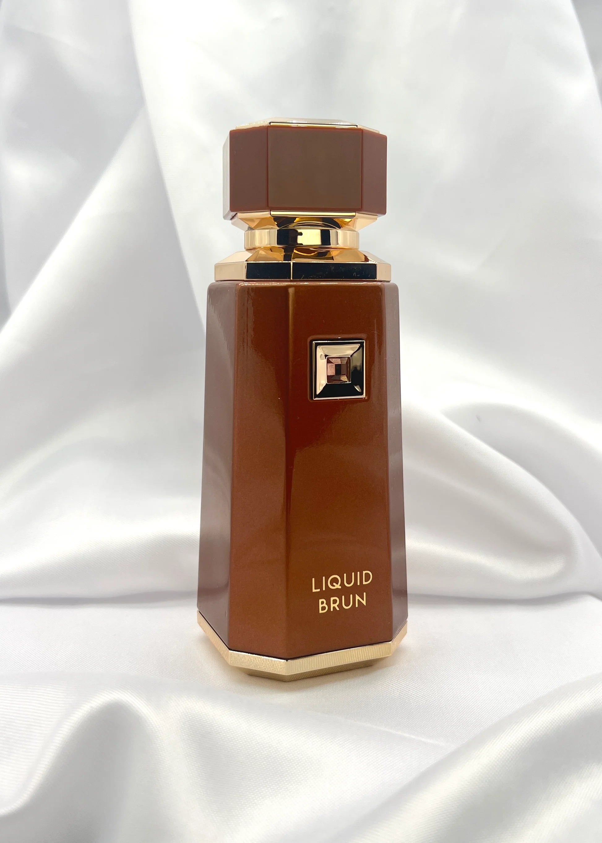 Brown perfume bottle labeled 'Liquid Brun' on a white fabric background