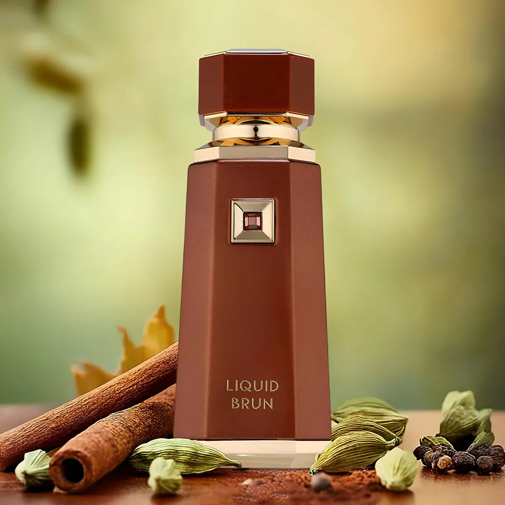 Brown perfume bottle labeled 'Liquid Brun' with cinnamon sticks and green leaves on a wooden surface.